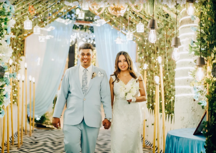 Couple walking down an aisle lined with greenery and hanging lights
